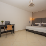 Habitación básica doble con cama doble y escritorio de trabajo junto a la ventana.