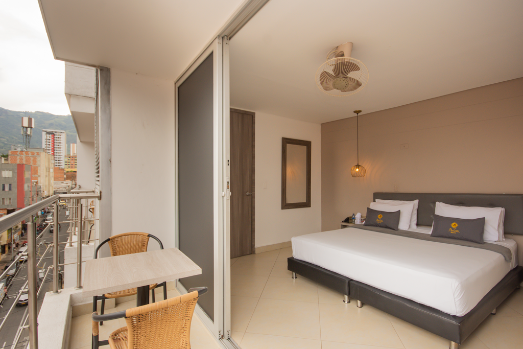 Habitación superior con balcón: cama doble, escritorio y salida al balcón con mesa y sillas.