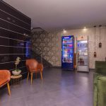 Zona de estar junto a la recepción, con sillones, nevera de bebidas y muro oscuro.