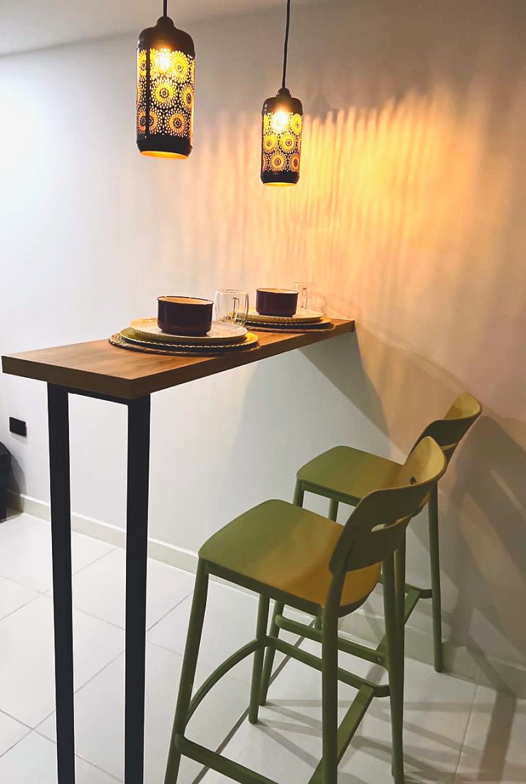 Barra de desayuno de madera con dos taburetes verdes y las lámparas caladas encendidas.