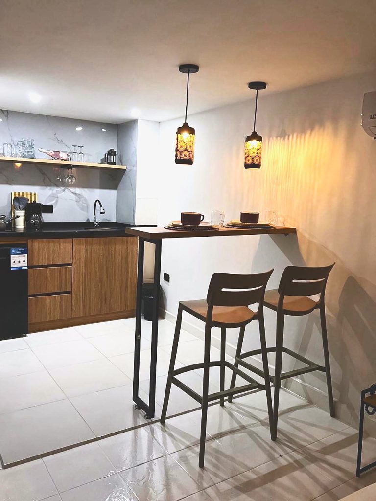Cocineta de la suite con barra de madera y dos taburetes, bajo lámparas caladas.