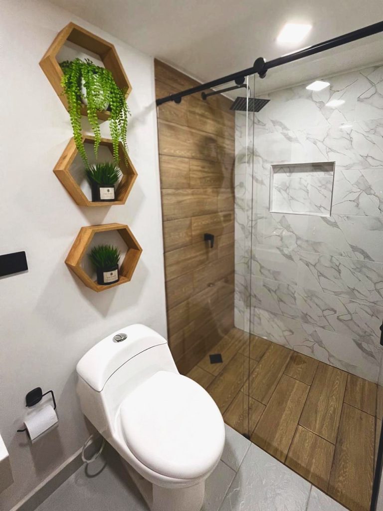 Ducha de la suite con puerta de vidrio, lluvia cenital y revestimiento en madera y mármol.