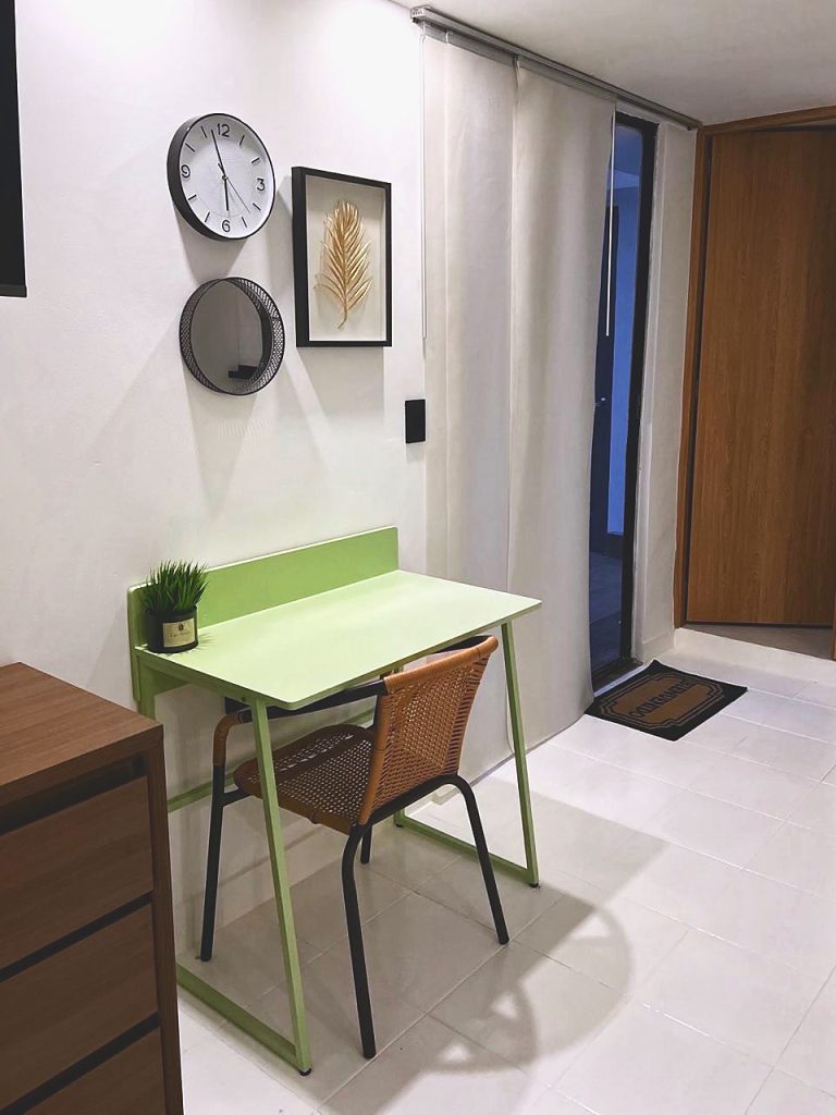 Escritorio verde con silla de mimbre junto a la entrada de la suite.